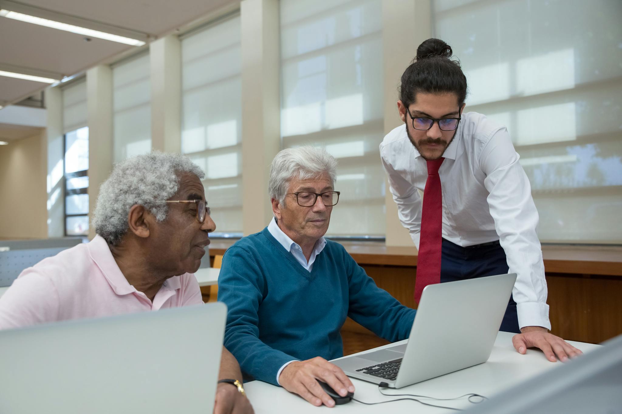 A diverse group of seniors learning with a tutor in a library, using laptops to study.