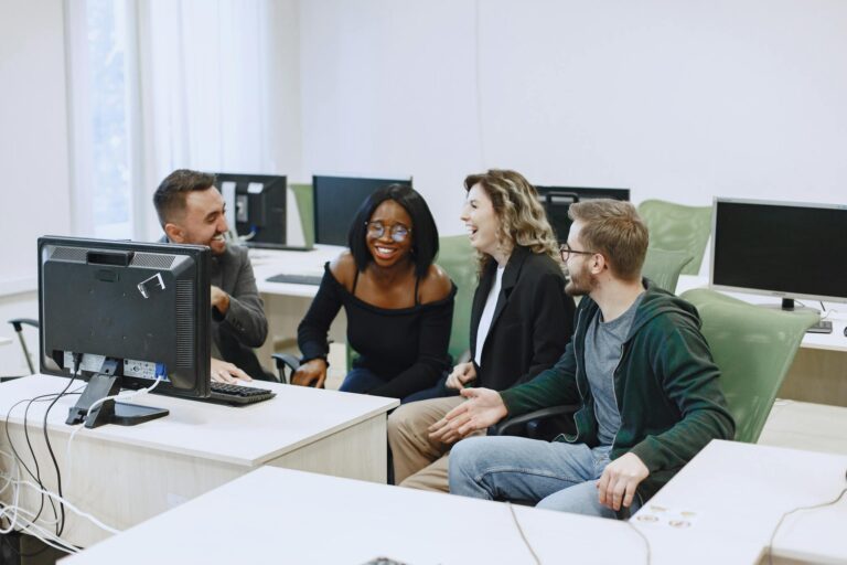Diverse group of young adults collaborating and laughing in a computer lab.