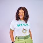 Joyful woman wearing NYSC uniform, smiling and posing indoors with a confident expression.